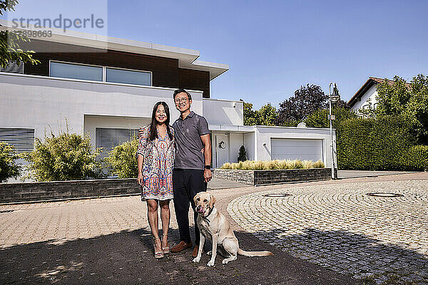 Happy couple with pet dog standing in front of house