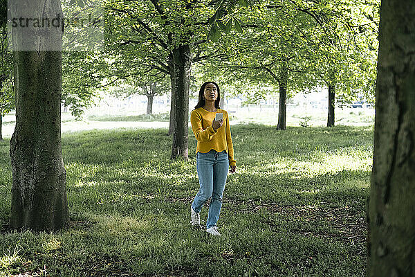 Junge Frau mit Smartphone geht im Park spazieren