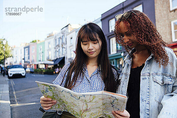 Lächelnde junge Freunde mit Karte stehen auf der Straße