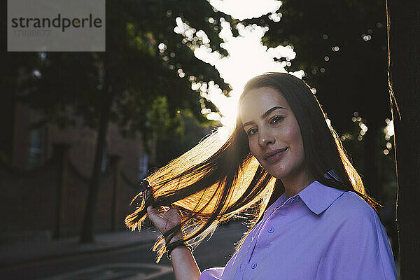 Schöne junge Frau mit der Hand im Haar auf der Straße bei Sonnenuntergang