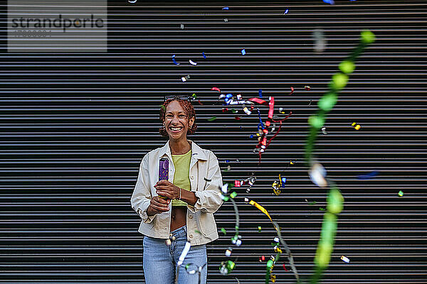 Happy woman with party popper enjoying in front of wall