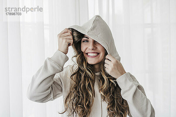 Fröhliche junge Frau trägt zu Hause ein Kapuzenshirt