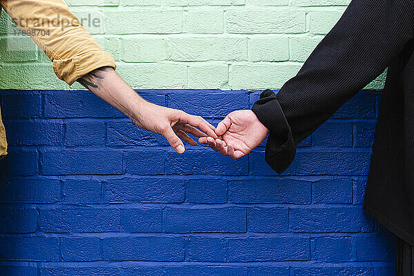 Schwule Männer halten sich an den Händen und stehen vor einer Mauer