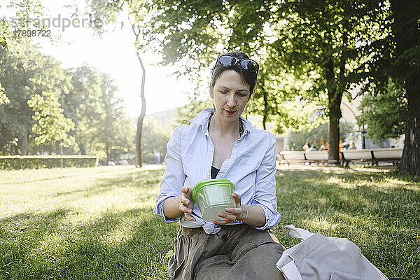 Frau mit Lunchbox sitzt an sonnigem Tag im Park