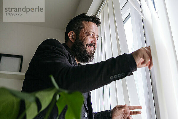 Lächelnder Geschäftsmann  der zu Hause aus dem Fenster schaut