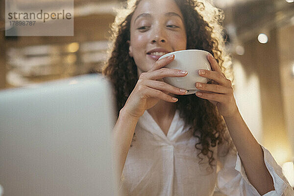 Lächelnde Geschäftsfrau mit Kaffeetasse und Blick auf den Laptop