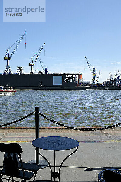 Deutschland  Hamburg  Tisch im Freien mit Kränen des Hamburger Hafens im Hintergrund