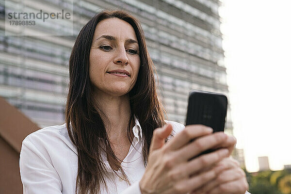 Reife Geschäftsfrau benutzt Smartphone auf Brücke vor Gebäudefassade