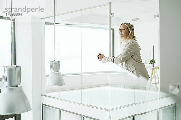 Geschäftsfrau lehnt am Geländer im minimalistischen Bürokorridor