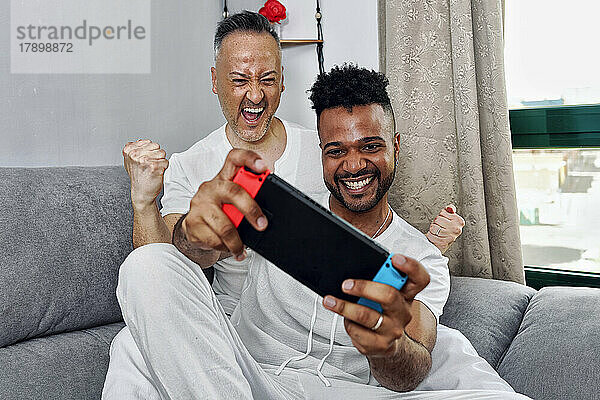 Glücklicher reifer Mann jubelt seinem Freund zu  der ein Videospiel spielt