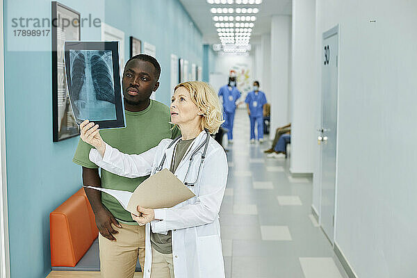 Reifer Arzt untersucht Röntgenaufnahmen mit Patient  der im Krankenhausflur steht