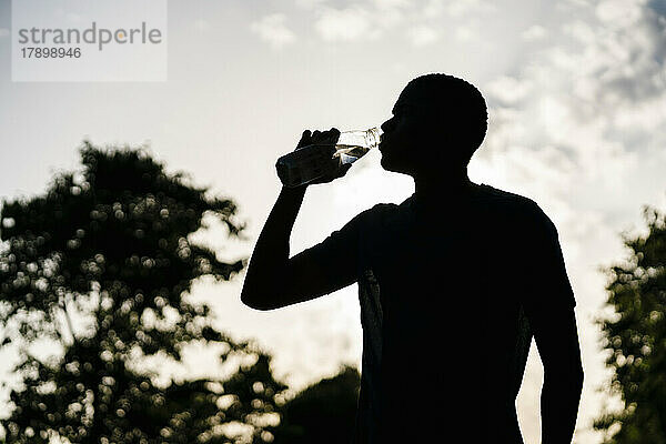 Young man drinking water at sunset