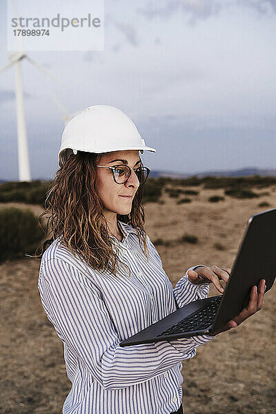 Konzentrierter Ingenieur mit Schutzhelm arbeitet am Laptop im Windpark