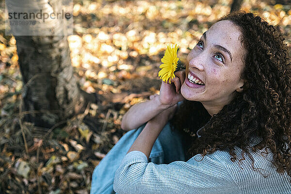 Glückliche junge Frau mit gelber Blume sitzt im Park