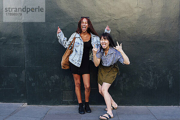 Cheerful woman enjoying with friend standing in front of wall