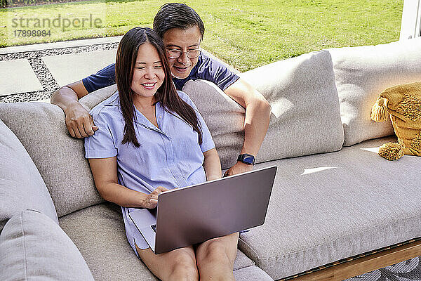 Lächelnder reifer Freiberufler teilt Laptop mit Mann  der sich auf Sofa lehnt