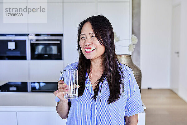 Glückliche Frau mit leerem Trinkglas  die zu Hause in der Küche steht