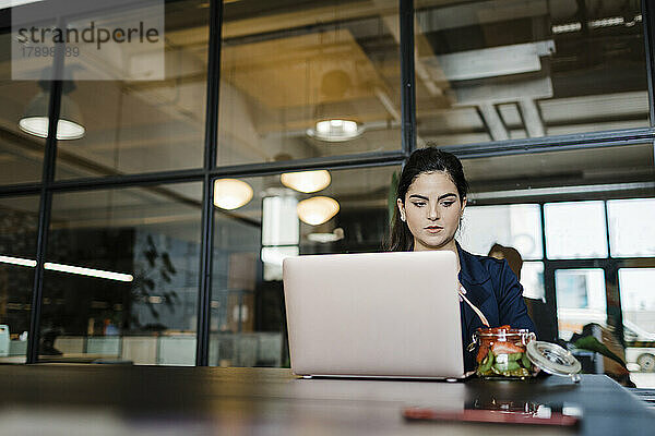 Junge Frau isst Früchte am Laptop im Büro