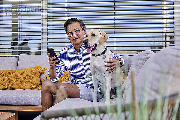 Smiling mature man with dog sitting on sofa