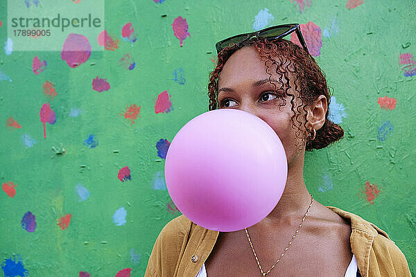 Young woman blowing bubble gum in front of wall