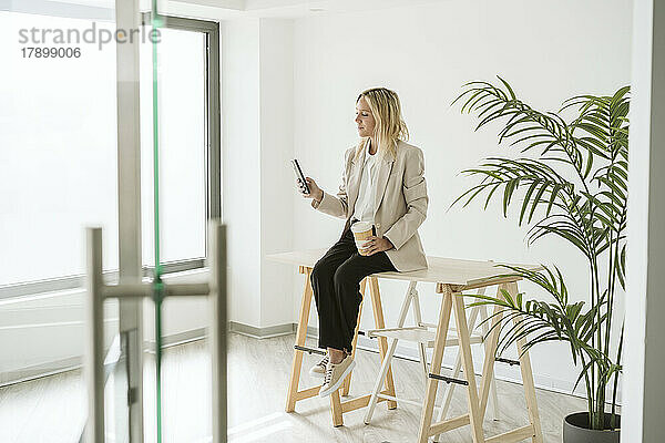 Geschäftsfrau sitzt am Schreibtisch im modernen Büro und benutzt Mobiltelefon