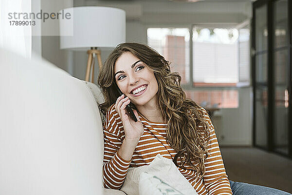 Glückliche junge Frau am Telefon im Wohnzimmer zu Hause