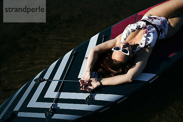 Frau mit Sonnenbrille liegt auf SUP-Board im See