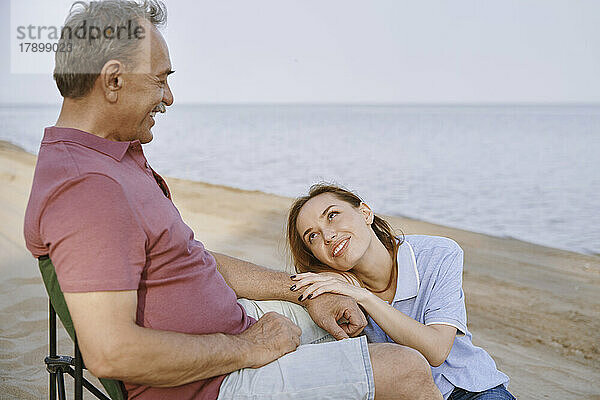 Vater spricht mit Tochter  die am Strand sitzt
