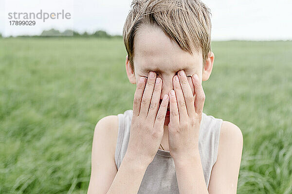Junge bedeckt Augen mit seinen Händen auf einer Wiese