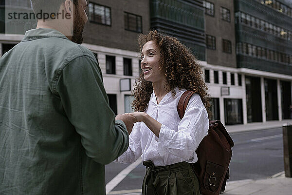 Lächelnde junge Frau hält Hand mit Mann am Fußweg