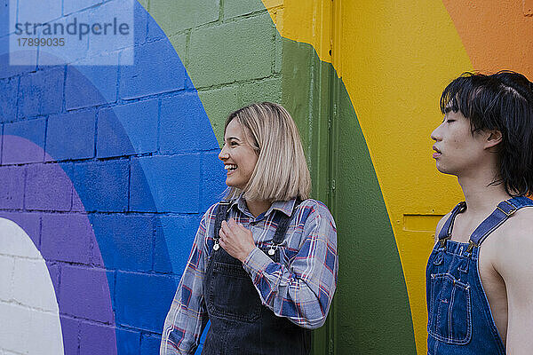 Glückliche junge Frau steht neben einer Freundin vor einem Regenbogenwandgemälde
