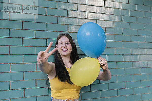 Frau hält blaue und gelbe Luftballons mit Friedenszeichen vor der Wand