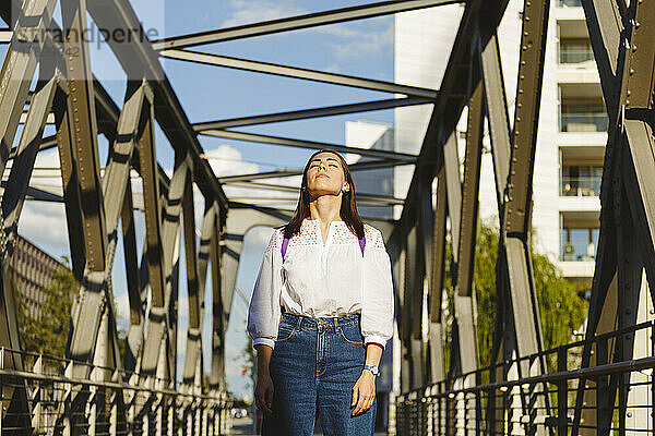 Frau mit geschlossenen Augen genießt das Sonnenlicht auf der Brücke