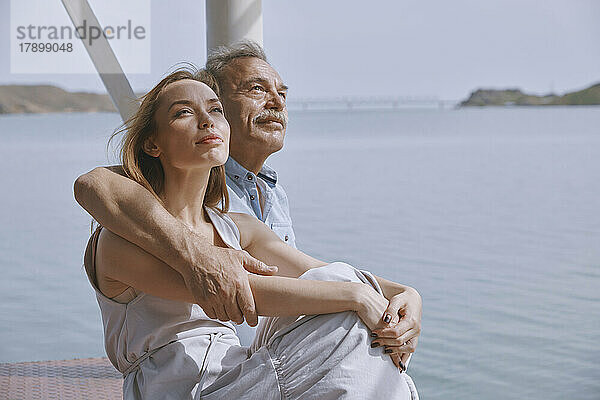 Nachdenklicher älterer Mann sitzt mit Tochter am Steg am Meer