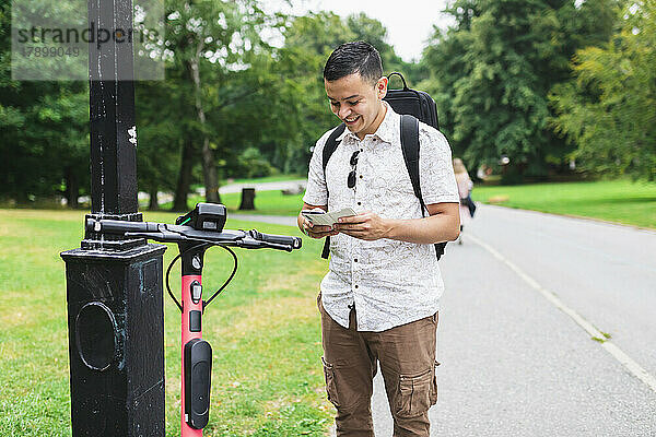 Mann benutzt Smartphone und steht neben Elektroroller im Park