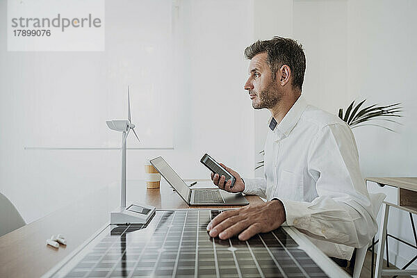 Ingenieur mit Hand am Solarpanel am Windturbinenmodell am Schreibtisch