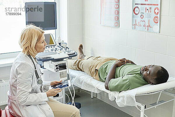 Arzt spricht mit Patientin  die im Bett liegt und in der Klinik Ultraschall macht