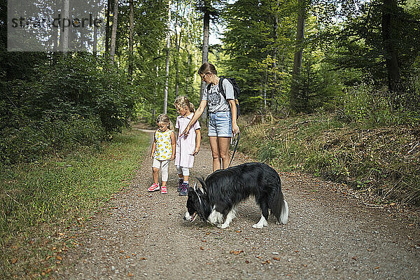 Frau mit Töchtern und Hund auf Fußweg im Wald