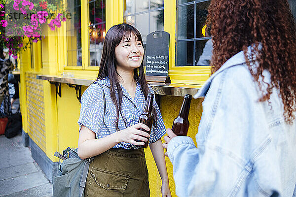 Fröhliche Freunde halten Bierflaschen in der Hand  die neben dem Restaurant stehen