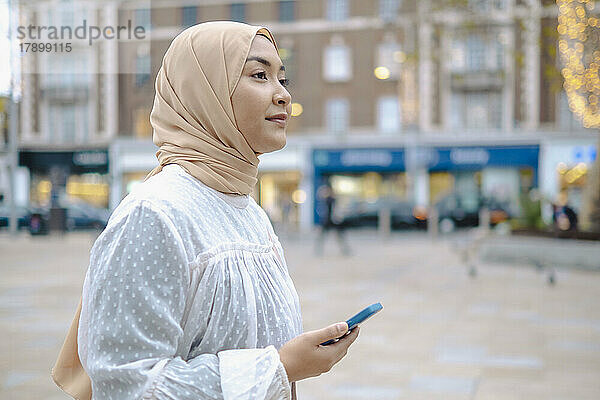 Nachdenkliche Frau mit Smartphone auf der Straße