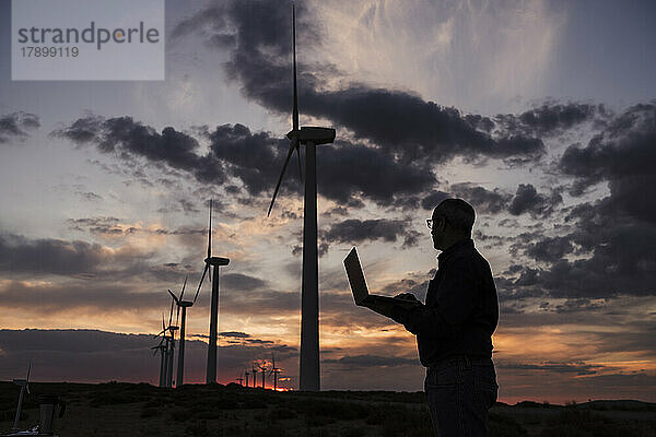 Silhouette eines Ingenieurs  der am Laptop im Windpark arbeitet