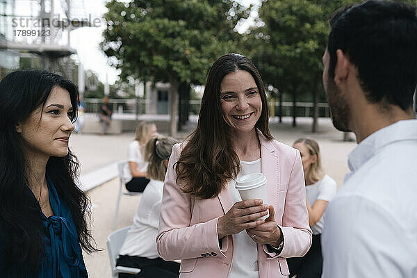 Geschäftsfrau mit Kaffeetasse diskutiert mit Kollegen im Büropark