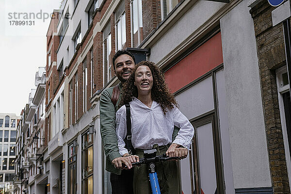 Glückliches Paar fährt mit Elektroroller vor dem Gebäude
