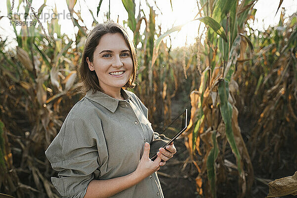 Porträt einer lächelnden Frau mit digitalem Tablet im Maisfeld