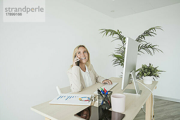 Lächelnde Geschäftsfrau am Telefon am Schreibtisch im Büro