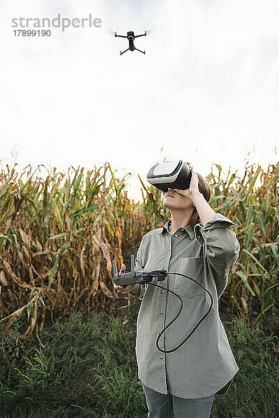 Frau mit VR-Brille und ferngesteuerter Drohne im Maisfeld