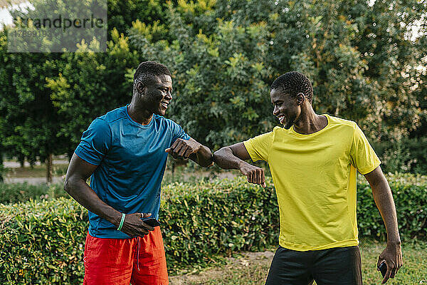 Happy young men greeting each other with elbow bump at park