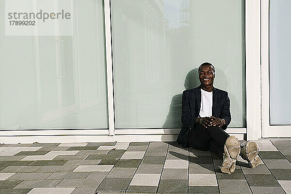 Happy young man sitting on ground in front of wall