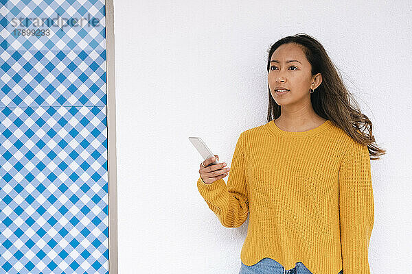 Junge Frau mit Smartphone steht vor der Wand