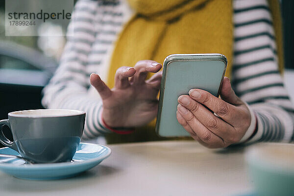 Frau benutzt Mobiltelefon und Tasse am Tisch im Café